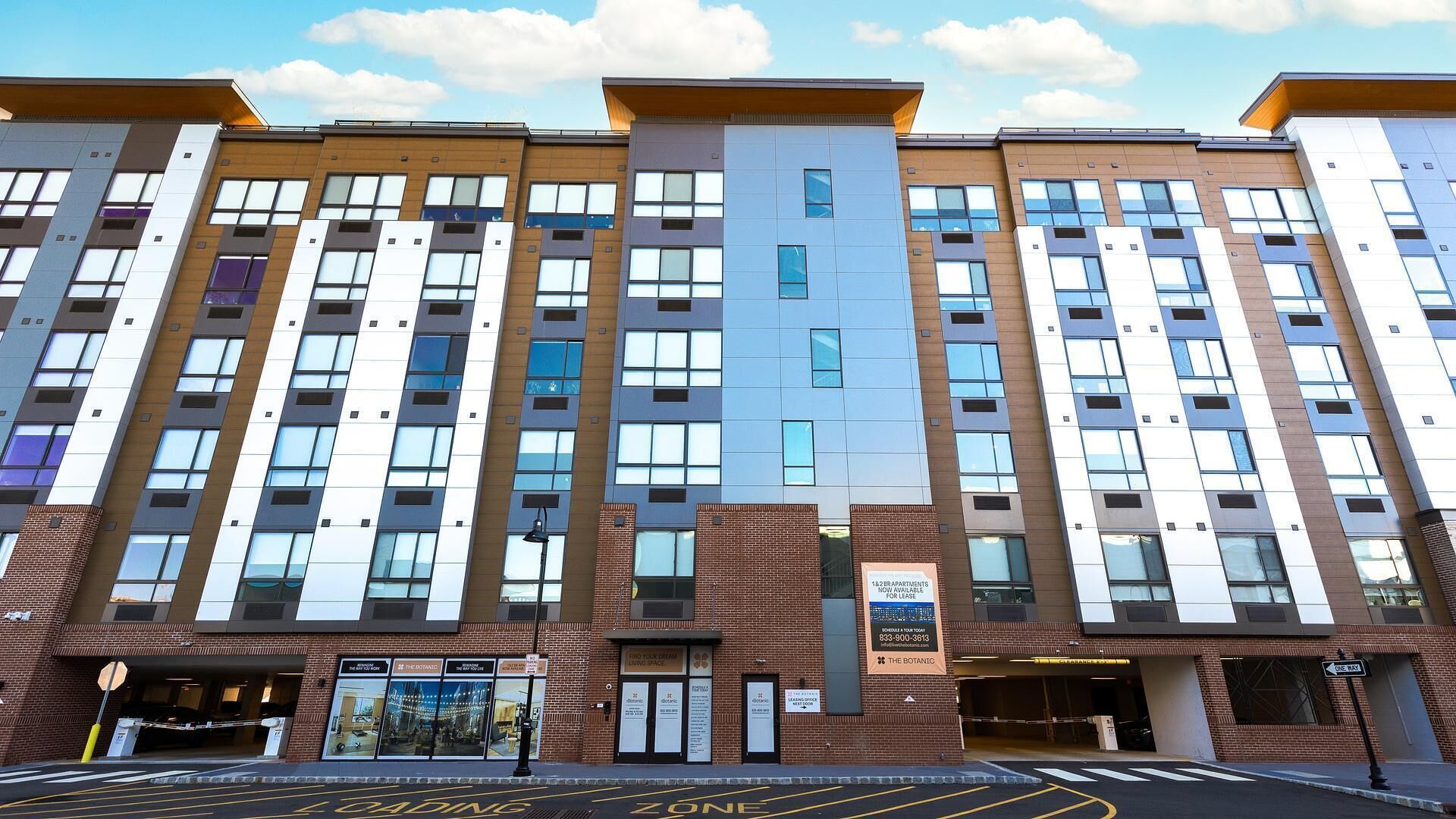 A multi-story hotel with a modern architectural design, featuring a mix of brick and glass facades, and a parking area marked with "Loading Zone" signs.