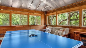 Una mesa de ping pong en una habitación con paredes de madera y ventanas grandes.