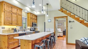Una cocina amplia con armarios de madera, una isla central con taburetes de bar, microondas y lavavajillas.