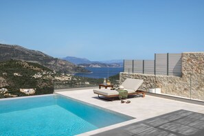 Uma piscina infinita moderna com vista clara para o mar e montanhas.