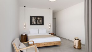 Un dormitorio moderno con una cama grande, una mesita de noche de madera, una silla, un adorno en la pared y un sombrero en un perchero.