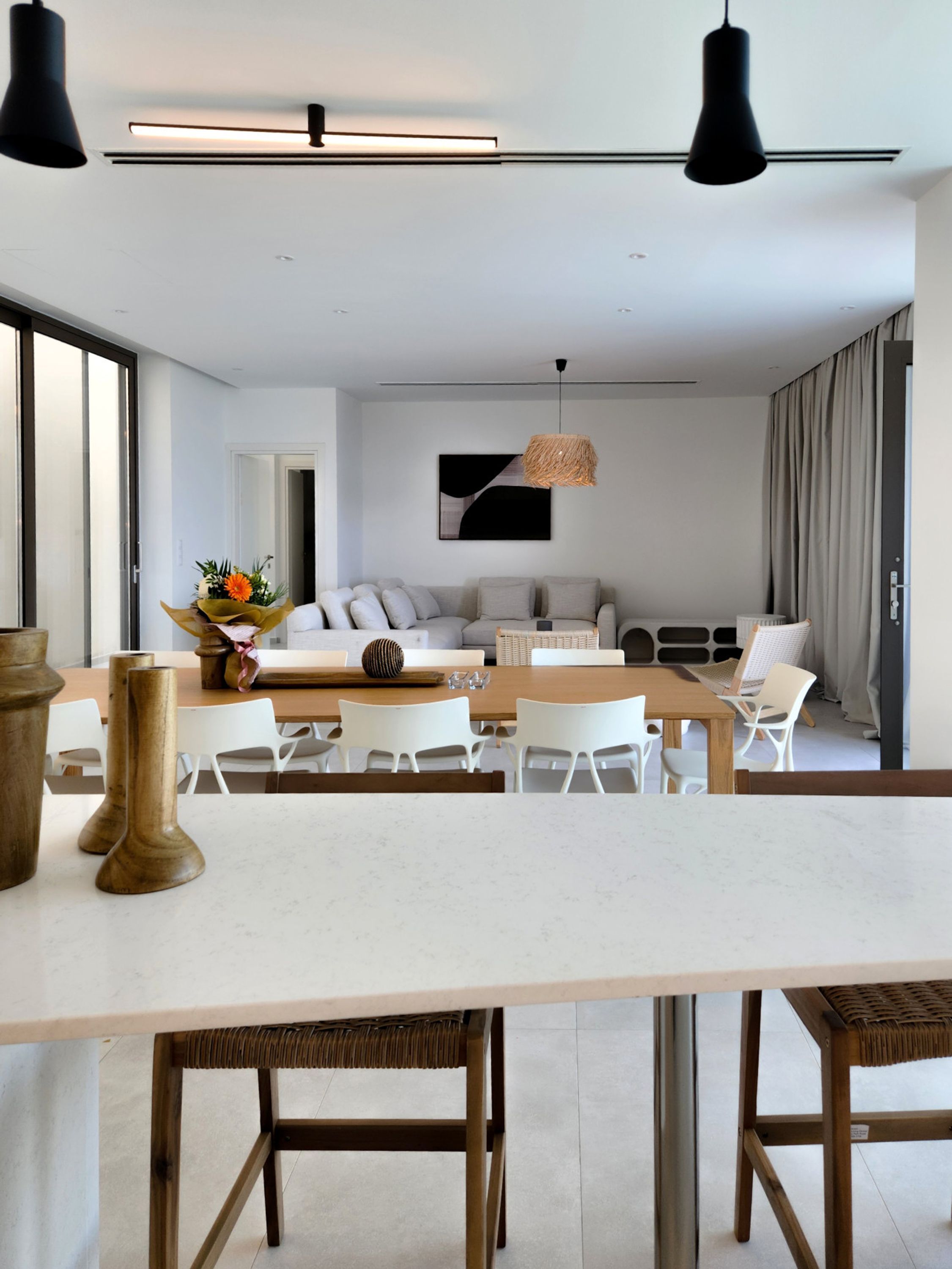 Un salon moderne avec un coin repas, comprenant une grande table, des chaises blanches et un canapé.