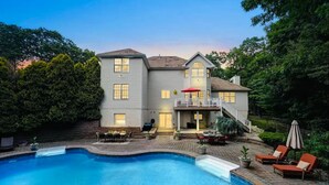 A two-story house with a swimming pool, outdoor furniture, and a covered patio area.