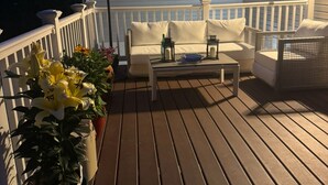 A wooden deck with a white railing, a sofa, a coffee table, and a striped umbrella.