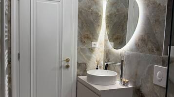 A bathroom with a white door, a round mirror with a light, a sink, and a toilet.