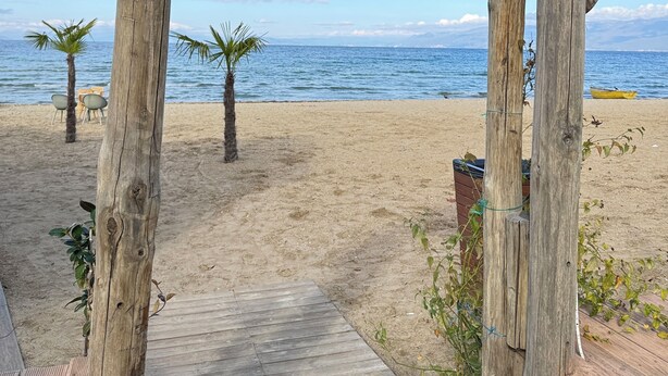 A wooden archway with a sign reading 'Beach-Bar' leading to a sandy beach with palm trees and a view of the sea. - Pogradec Luxe Apartment (Pogradec)