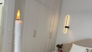 Un dormitorio con cama, mesita de noche, lámpara de pared y una vela encendida.