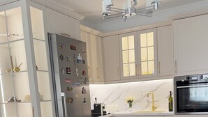 A modern kitchen with white cabinetry, a built-in refrigerator, a stove, and a dining area with a sofa and a coffee table. - Pogradec Luxe Apartment (Pogradec)