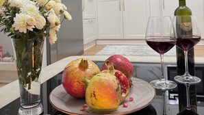 A kitchen with white cabinets, a marble countertop, a refrigerator, a plate with fruits, two wine glasses, and a candle. - Pogradec Luxe Apartment (Pogradec)