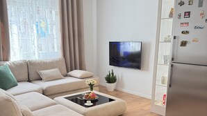 A modern living room with a sectional sofa, a coffee table, a flat-screen TV, a refrigerator, and decorative magnets. - Pogradec Luxe Apartment (Pogradec)