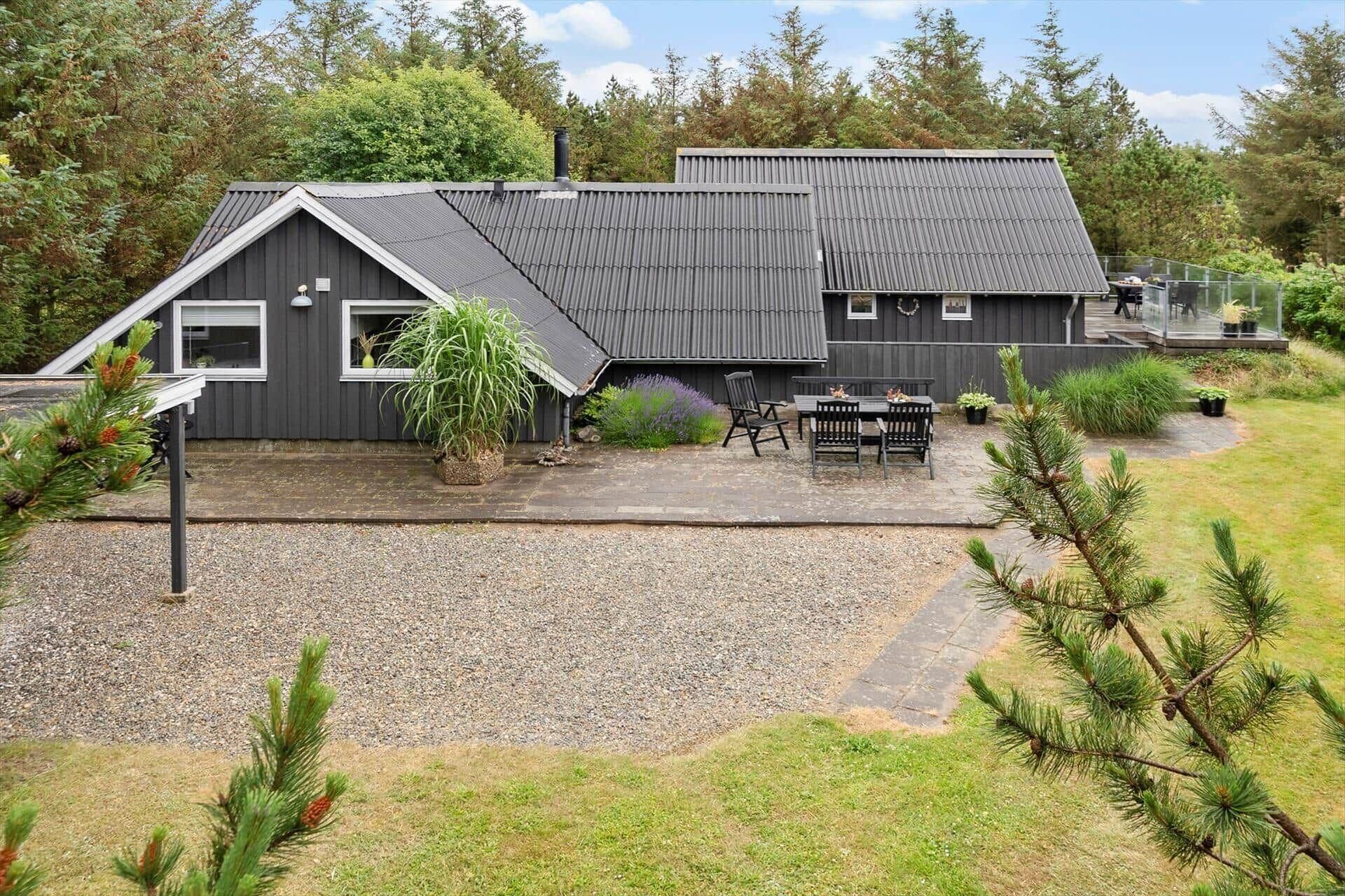 A modern building with a sloped roof, a patio area with outdoor seating, and a gravel driveway.