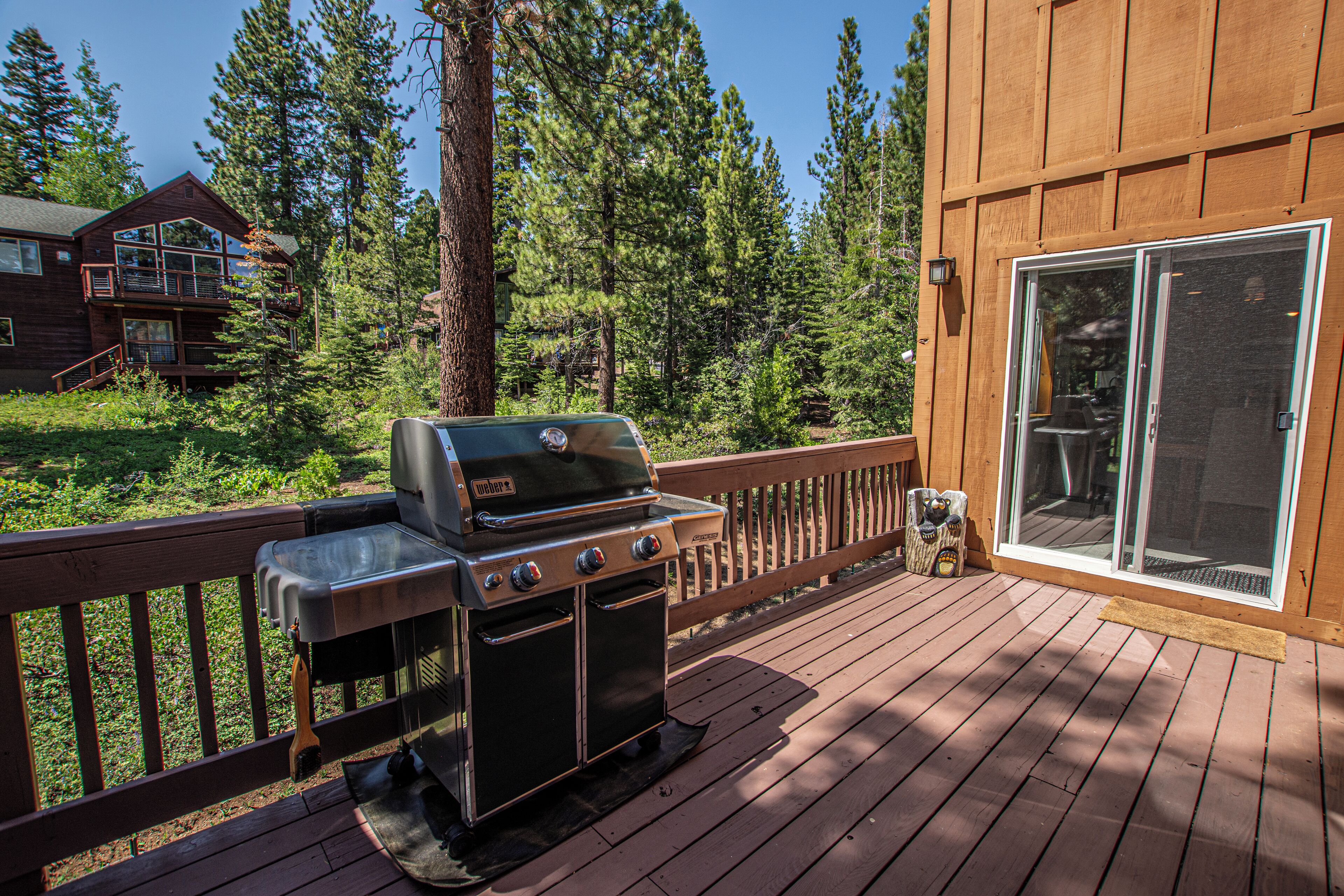 A deck with a grill, a wooden fence, and a view of a forest.