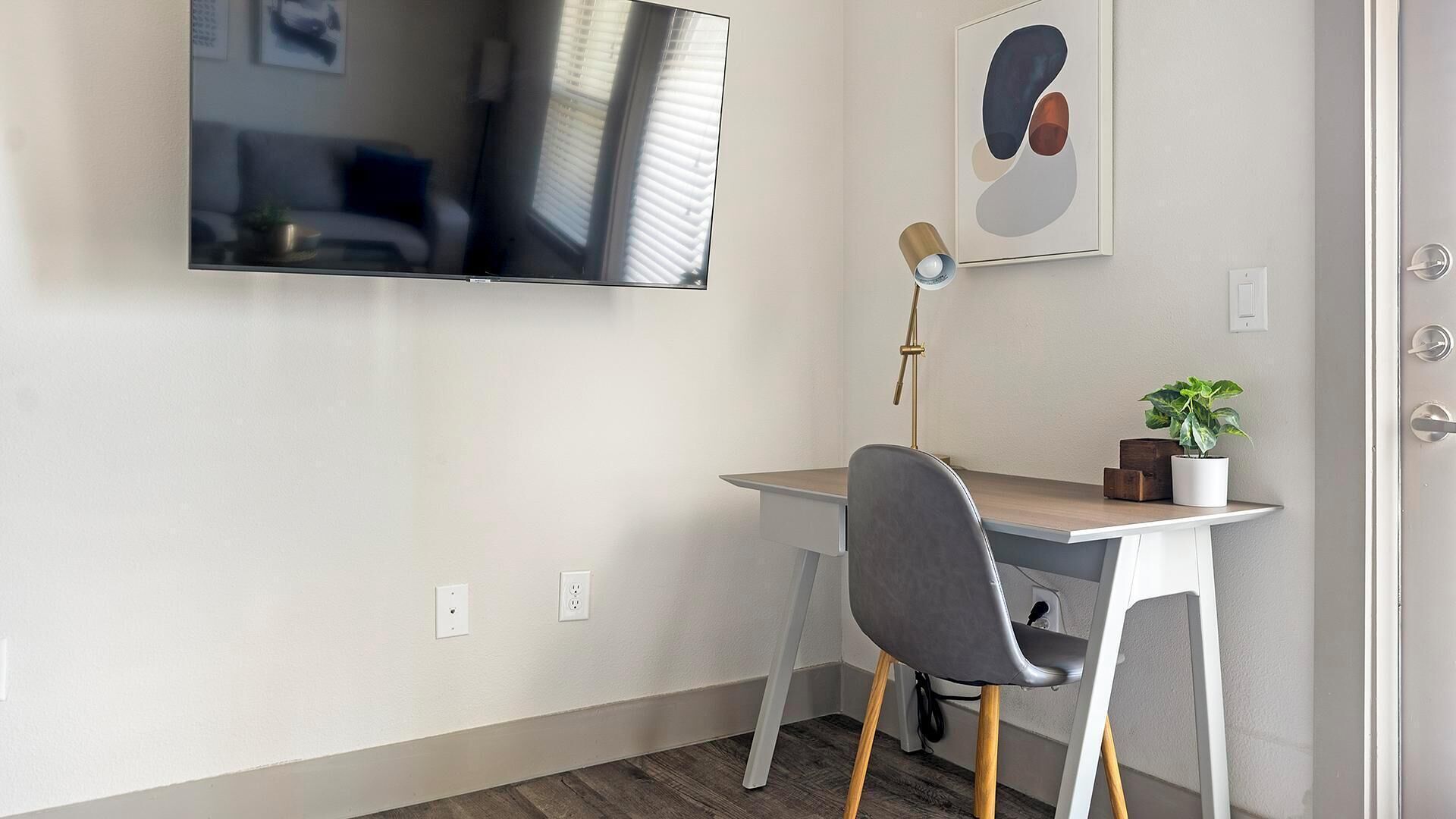 Un espace de bureau moderne comprenant un bureau, une chaise et un téléviseur fixé au mur.