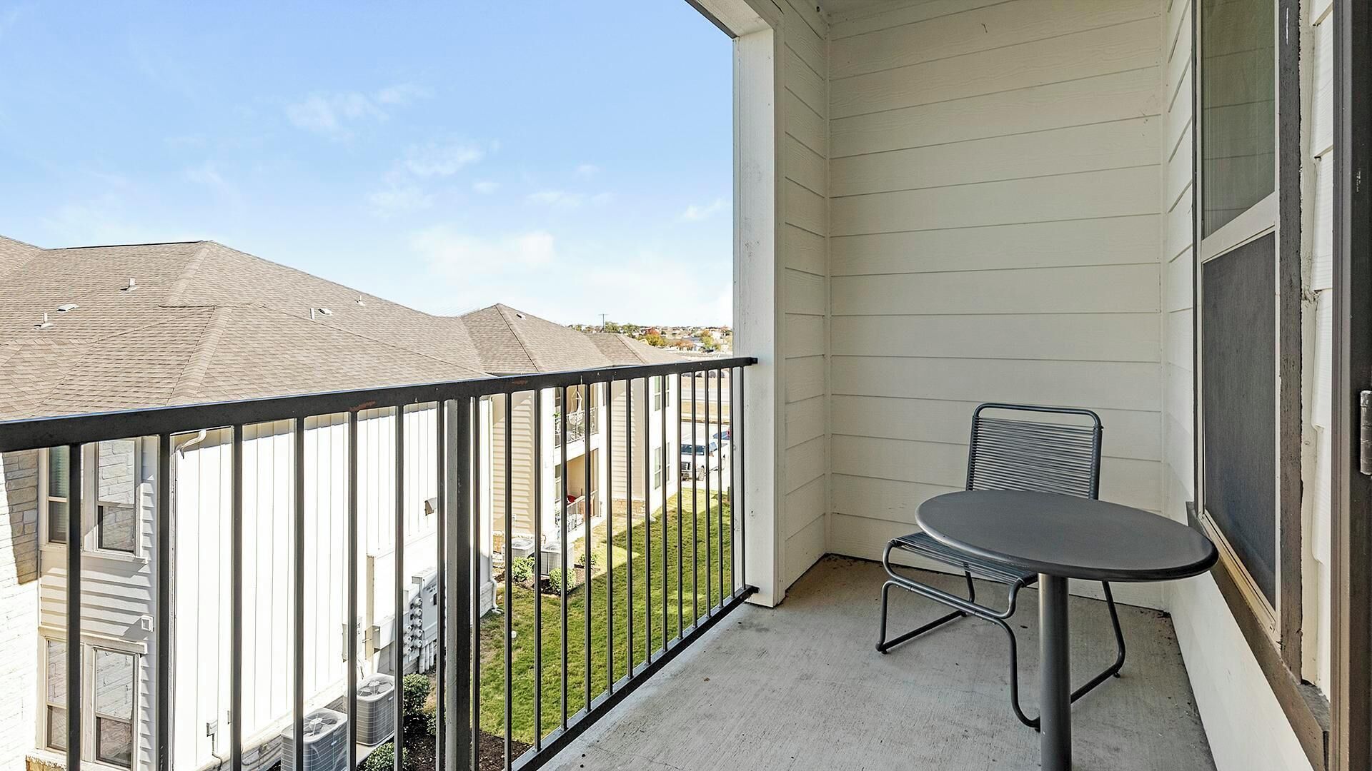 A balcony with a metal railing, a small round table, and two chairs.