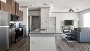 A modern kitchen with granite countertops, stainless steel appliances, and a central island with a sink. - Landing | Amazing 1BD, Gym, Clubhouse (Manor)