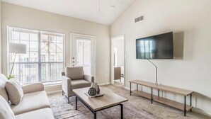 Una sala de estar moderna con sofá, sillón, mesa de centro, televisión y un banco.