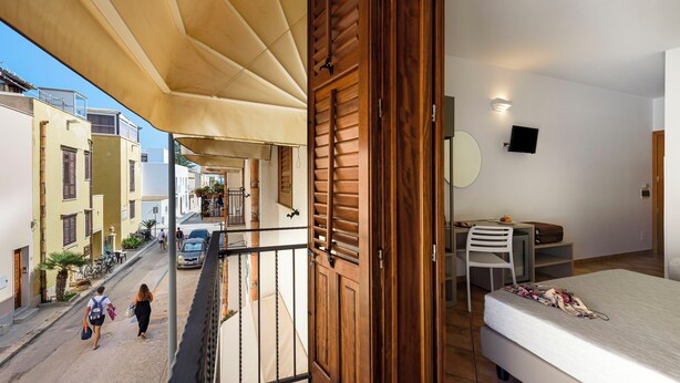 Een balkon met een houten deur, een bed, een bureau en een stoel.