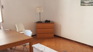 Huoneessa on puinen pöytä, valkoiset tuolit, pieni puinen lipasto ja lamppu.