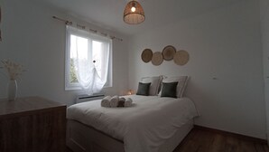 Une chambre à coucher comprenant un lit, une table de chevet, une fenêtre avec des rideaux, un luminaire suspendu et des éléments de décoration murale.