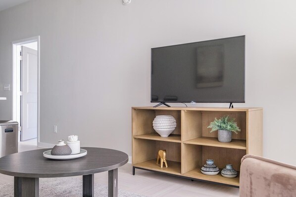 Una sala de estar moderna con una mesa redonda, un mueble de televisión de madera con estantes y un televisor de pantalla plana montado en la pared.