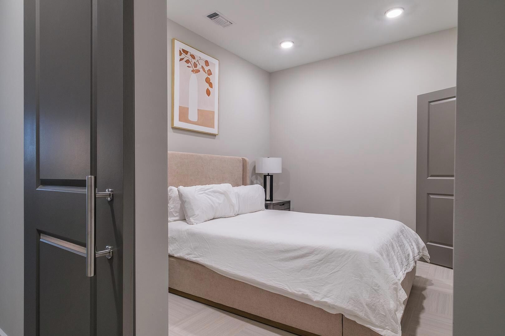 Un dormitorio con cama, mesita de noche, lámpara y puerta.