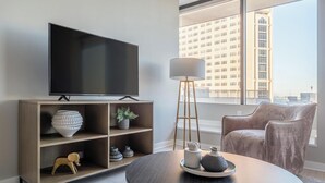 A modern living room with a flat-screen TV, wooden shelving, a round coffee table, and a city view. - Landing | Chic 3BD in Fountain Heights (Birmingham)