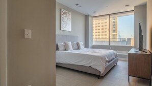 A modern bedroom with a large bed, a desk, and a window with a city view. - Landing | Chic 3BD in Fountain Heights (Birmingham)