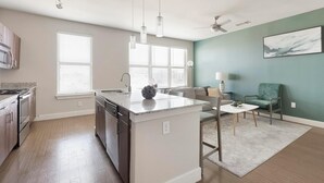 Une cuisine moderne dotée d’un îlot central, un coin repas avec une table et des chaises, et un espace de vie comprenant un canapé et un fauteuil.