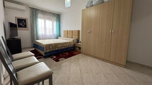 Ein Schlafzimmer mit Bett, Kleiderschrank, Schreibtisch, Stuhl und Fernseher.