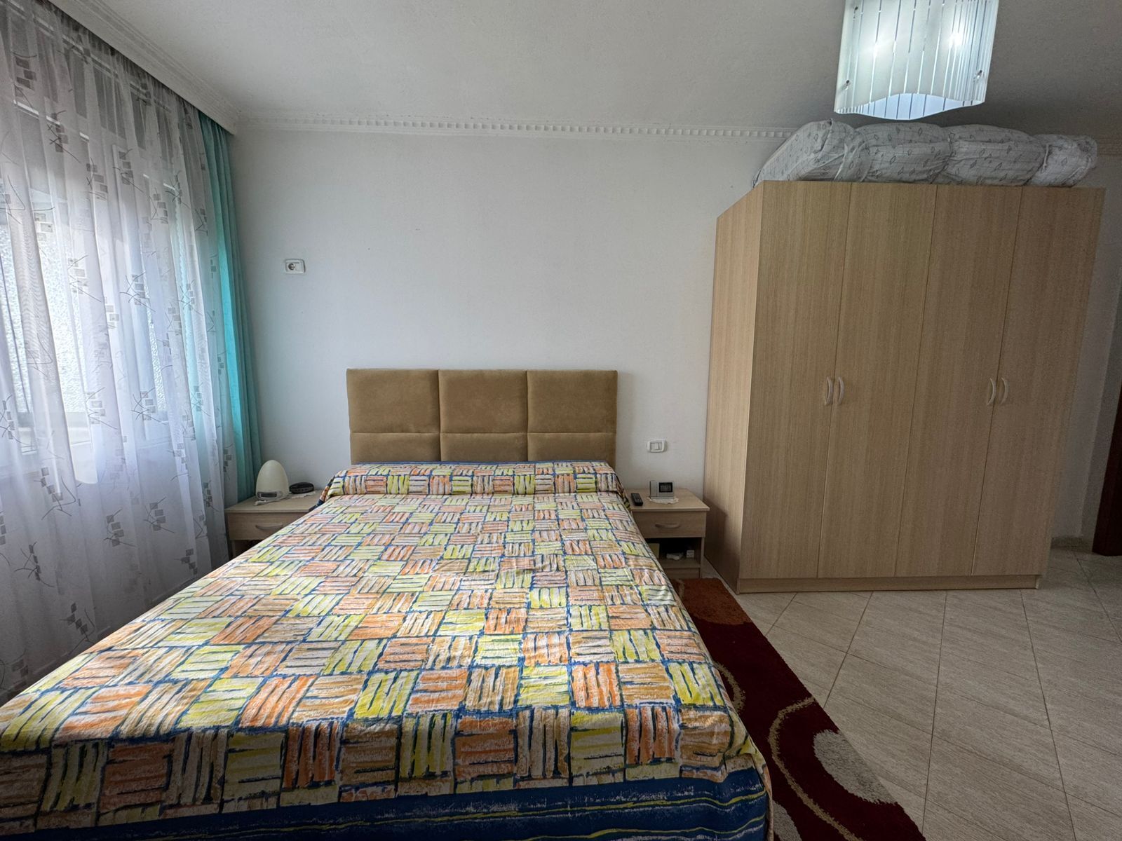 Een slaapkamer met een bedovertrek met patroon, een houten garderobe, een nachtkastje en een nachttafel.