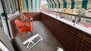 Ein Balkon mit Blick auf die Stadt, ausgestattet mit einem Tisch, Stühlen, einer gepolsterten Bank und gestreiften Vorhängen.