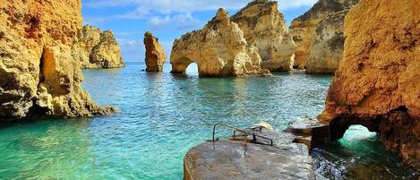 A coastal scene with clear turquoise waters, rocky formations, and a stone platform with a railing.