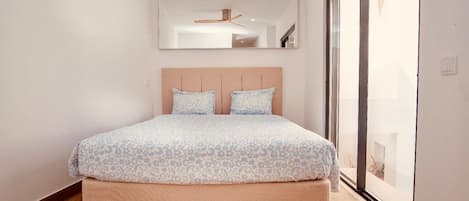 A bedroom with a bed, a ceiling fan, a large mirror, and a sliding glass door.