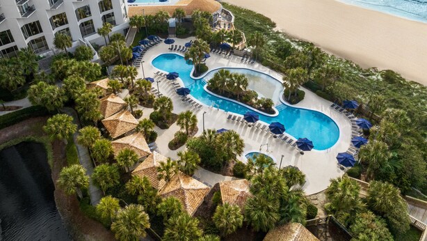 Vue aérienne d’un complexe hôtelier doté de plusieurs piscines, d’une plage et d’un immeuble de grande hauteur.