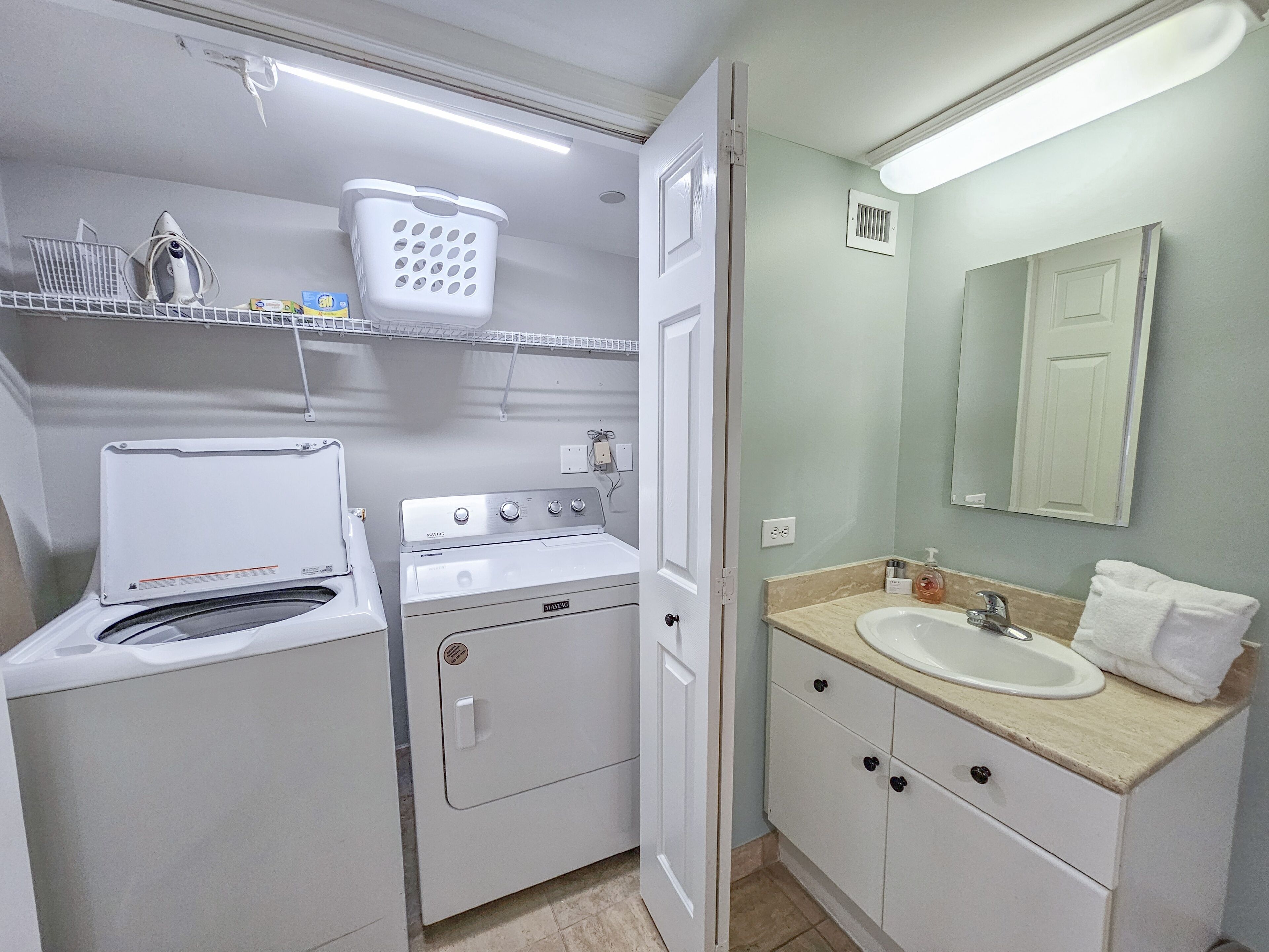 A compact laundry room with a washing machine, dryer, and a small shelf with laundry supplies.