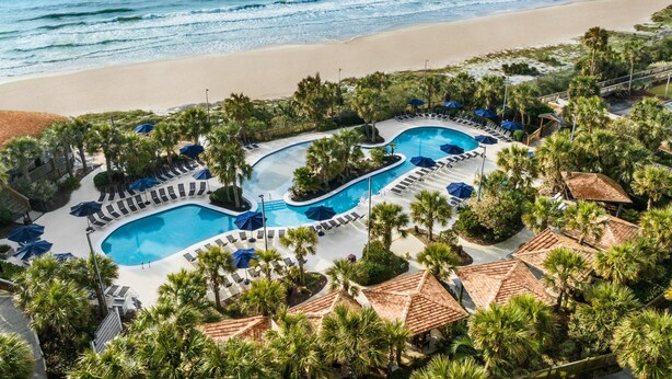 Un resort con area piscina, lettini e vista sulla spiaggia.