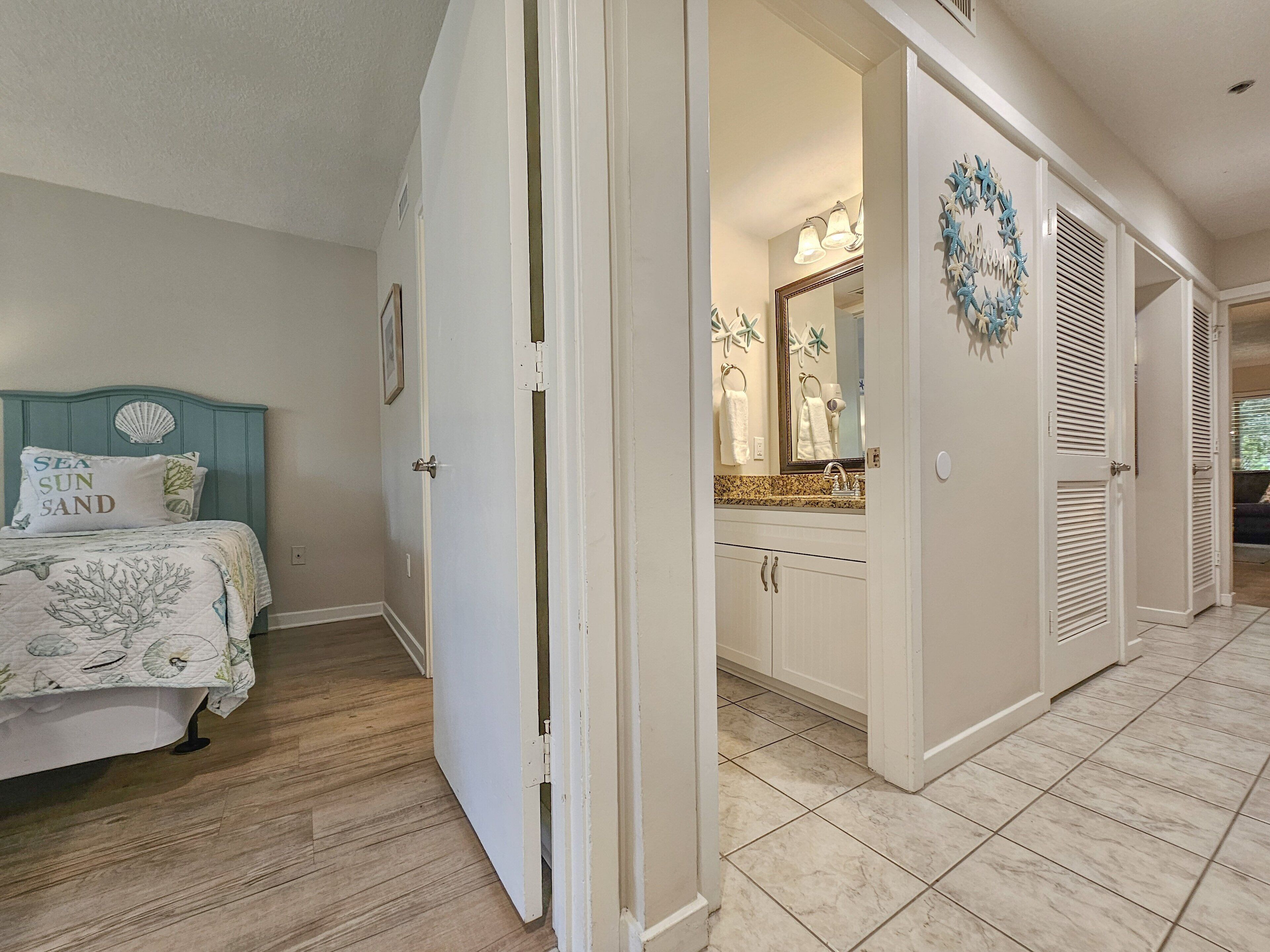 Une chambre à coucher comprenant un lit, une table de chevet, une commode et une salle de bain avec un lavabo, un miroir et un porte-serviettes.