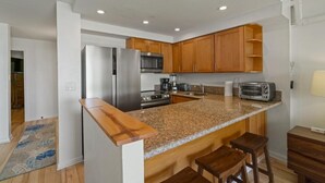 Et moderne køkken med granitbordplader, træskabe, rustfrie stålgre og en bar med barstole.
