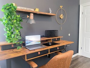 A modern workspace with a laptop, a desk lamp, a plant, and a wall clock.