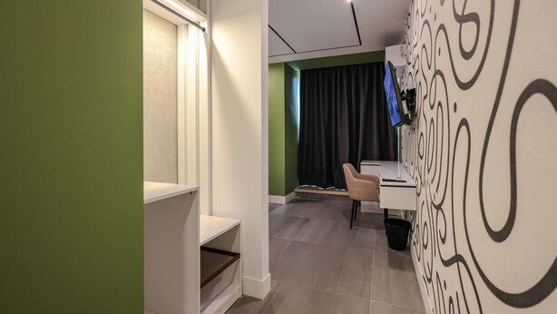 A modern hotel room with a green wall, a white cabinet, a desk with a chair, and a patterned wall. - Grandstay Studio 111 (Durrës)