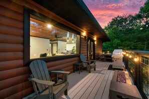 A wooden deck with Adirondack chairs, a grill, and string lights.