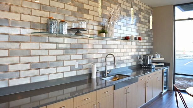 A modern kitchen with a brick backsplash, stainless steel appliances, and a large window offering a view of the outdoors. - Landing | Spectacular 1BD, Gym, Game Room (Edwardsville)