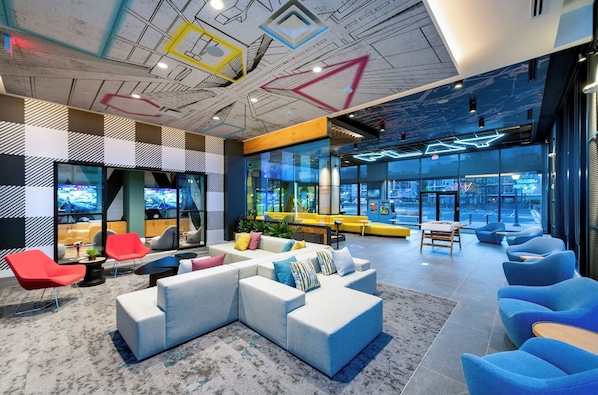 A modern lobby with a sectional sofa, red chairs, and a large window offering a city view.