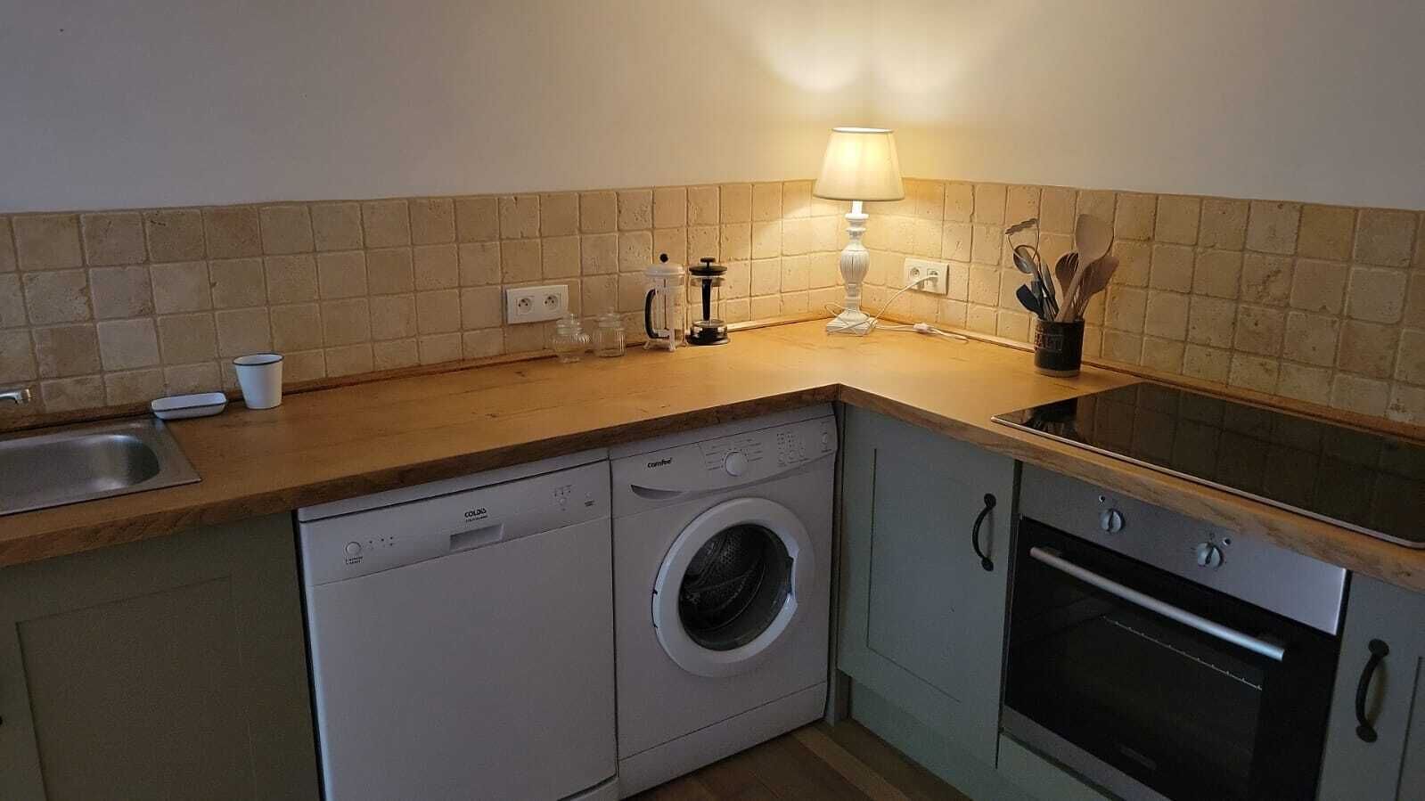A compact kitchen with a dishwasher, washing machine, and oven. There is a countertop with a lamp and a cup.