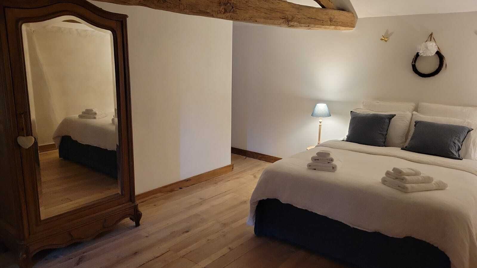 Et soveværelse med et stort spejl, en seng med hvide sengetøj, en sengetøjslampe og en rund dekoration på væggen.