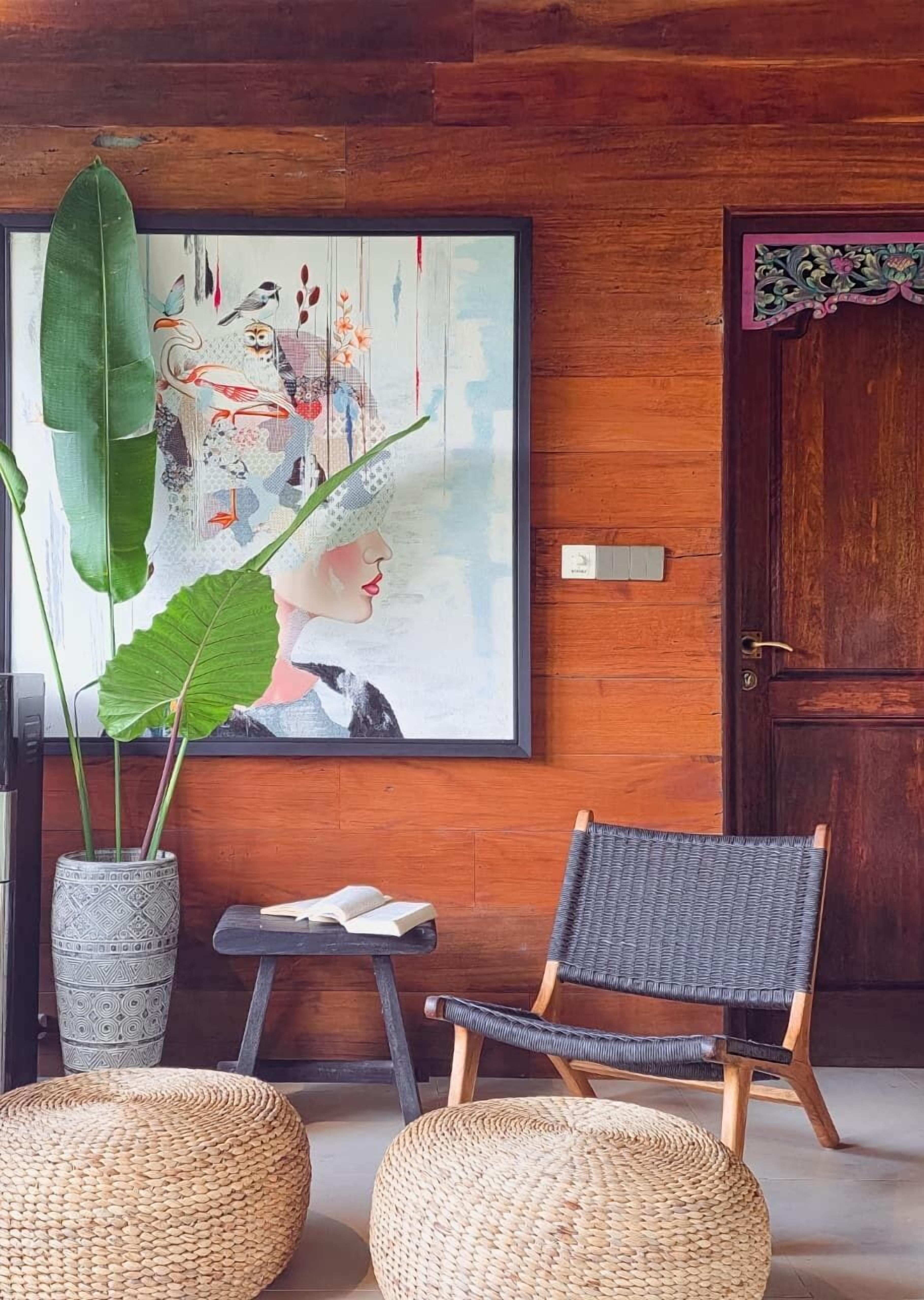 A room with a large abstract painting, a potted plant, a wicker chair, and a small table with an open book.