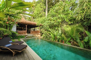 A pool with lounge chairs and a wooden structure surrounded by lush greenery. - Villa Dharuna Ubud (Ubud)