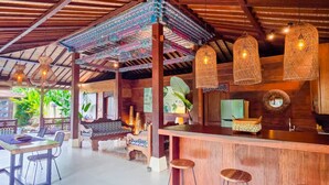 A bar area with a wooden counter, stools, and hanging wicker lamps. - Villa Dharuna Ubud (Ubud)