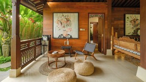 A wooden-floored room with a woven bench, a chair, and a small table with books. - Villa Dharuna Ubud (Ubud)