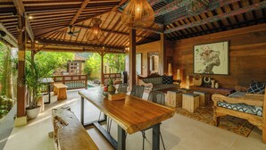 A spacious indoor area with a wooden dining table, chairs, and a sofa. There are hanging light fixtures and a decorative ceiling. - Villa Dharuna Ubud (Ubud)